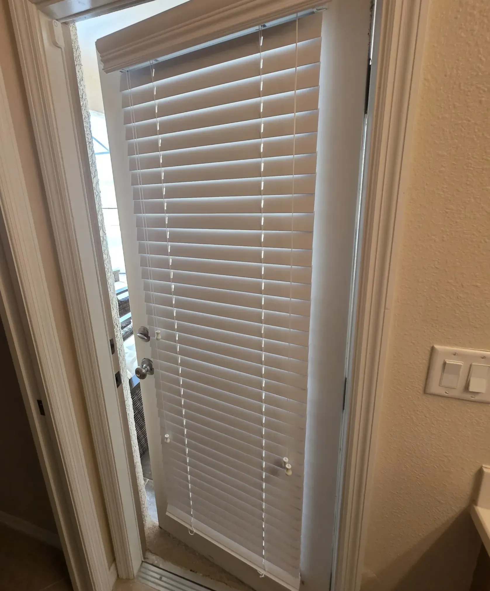 Bathroom exterior door with white blinds stands ajar, revealing the pool deck as morning light seeps in - an unexpected open door discovered at 6:49 a.m.